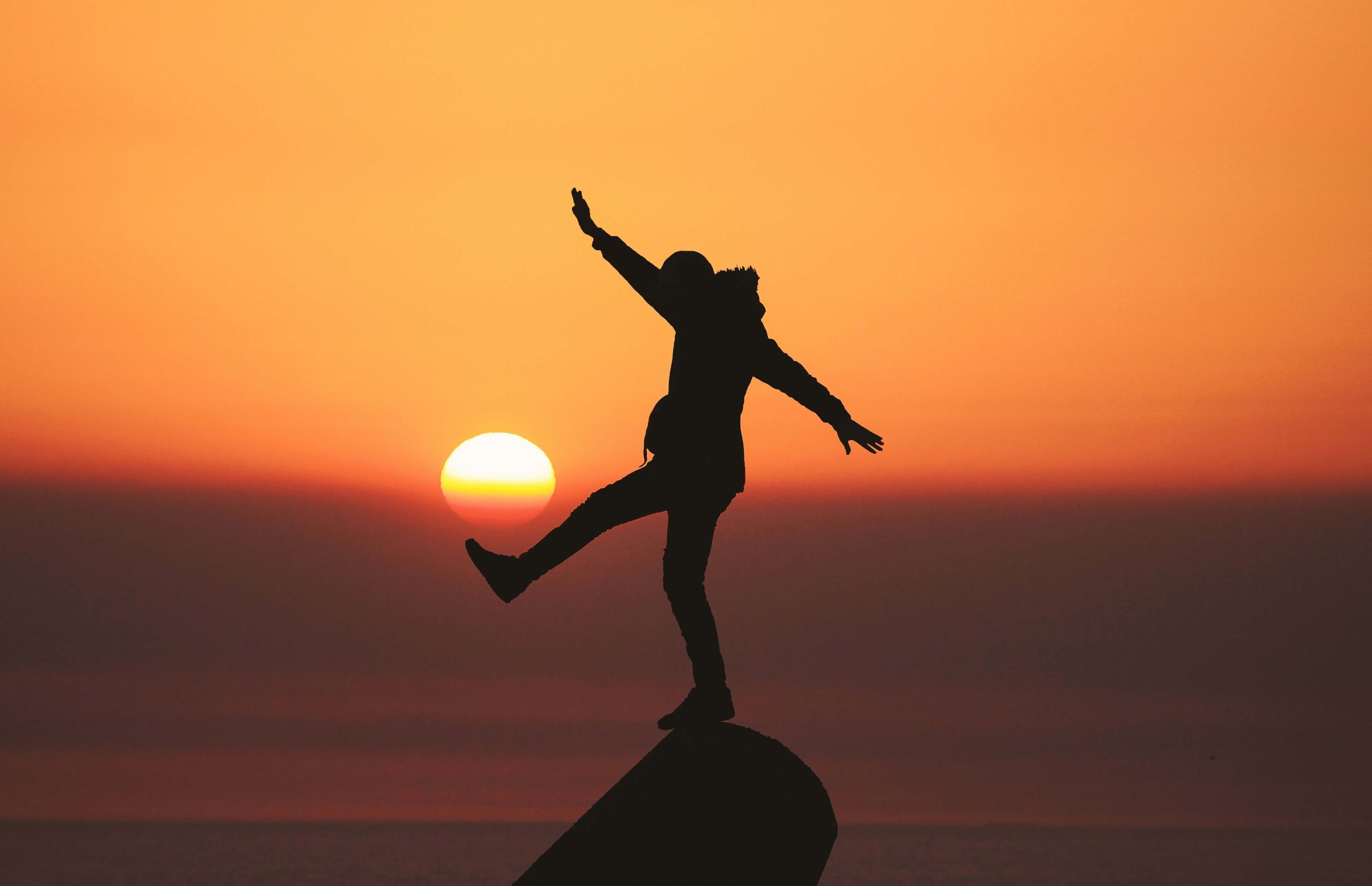 Silhouette of a person joyfully balancing on a rock at sunset.